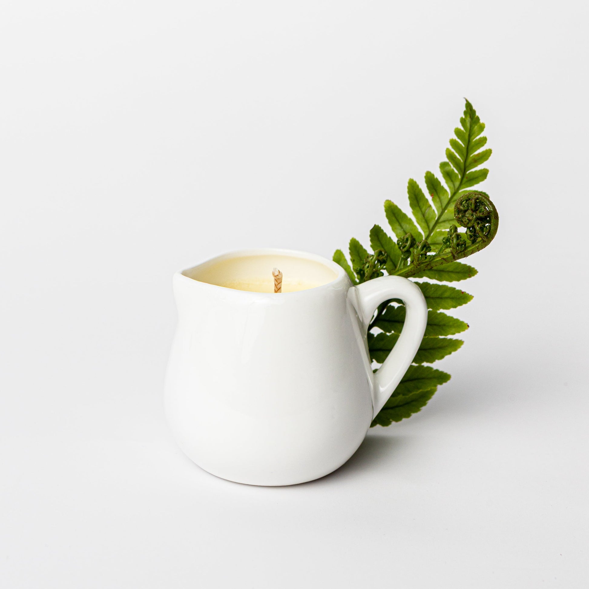 White cream cup with a lit candle and a green leaf on a white background