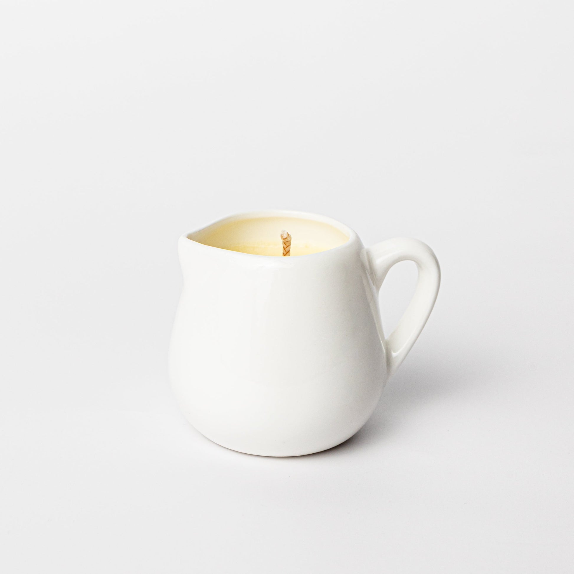 White ceramic pitcher with a candle on a light gray background