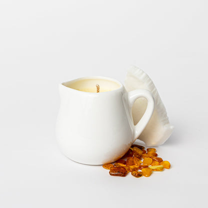 White ceramic mug with a lit candle inside, surrounded by amber-colored stones on a light gray background