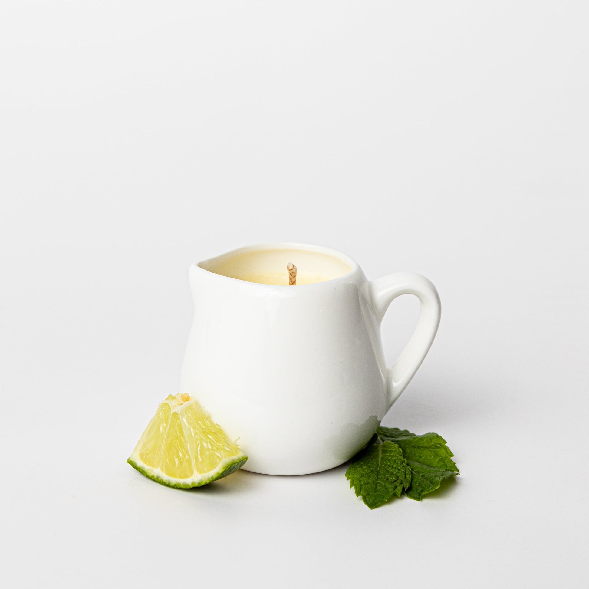 White ceramic mug with a lit candle, lime wedge, and mint leaves on a white background