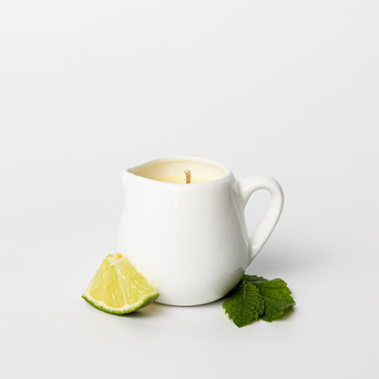 White ceramic mug with a lit candle, lime wedge, and mint leaves on a white background